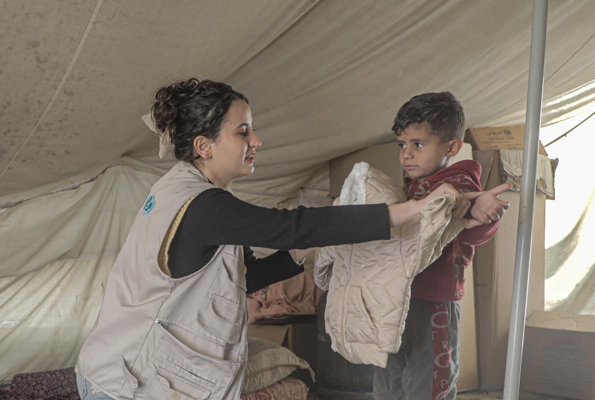 UNICEF staff member helps a young child unpack winter clothing distributed for children aged 3 to 5 years old in central Gaza in the State of Palestine.