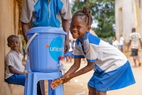 Une fille sourit à l’objectif en se lavant les mains à un robinet de l’UNICEF.