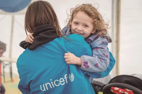 In Romania, a girl smiles at the camera while being carried by a UNICEF worker.  