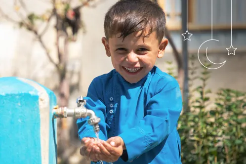 Un jeune garçon se lave les mains tout en souriant à l’objectif.