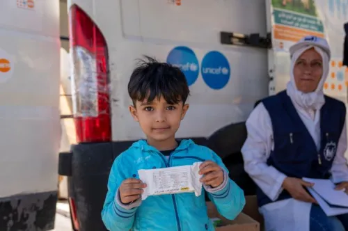 A child looking directly at the camera with a calm expression while holding up a packet of therapeutic food at a UNICEF centre.