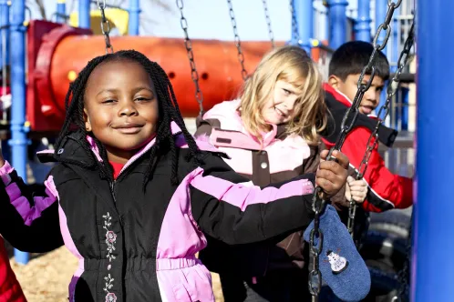 Trois enfants d’horizons différents sont assis sur des balançoires dans un parc.