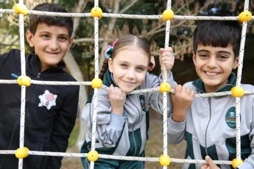 Trois enfants souriants se tiennent ensemble sur un terrain de jeu au Liban.