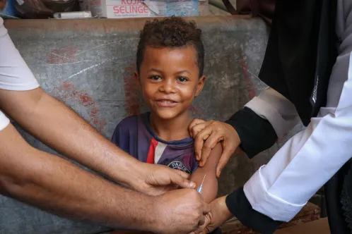 A young boy smiles at the camera while getting vaccinated.