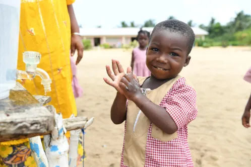 A young boy smiles at the camera while washing his hands.