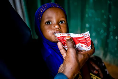 Un jeune enfant dans les bras de sa mère mange le contenu d’un sachet d’aliment thérapeutique prêt à l’emploi.