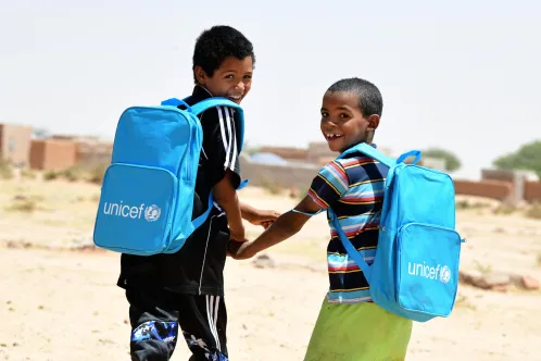 Dans le nord du Niger, deux enfants rient et marchent ensemble en portant leurs nouveaux sacs à dos de l’UNICEF remplis de fournitures scolaires.