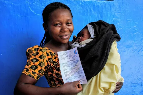 Une mère souriante tient son bébé et un acte de naissance en République démocratique du Congo.