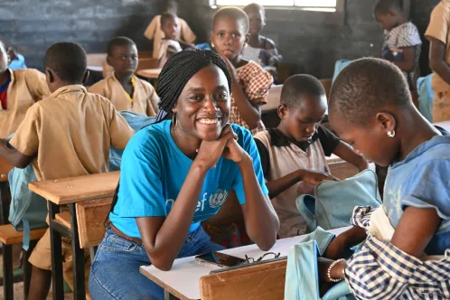 Une employée de l’UNICEF sourit assise au milieu d’élèves dans une école de la Côte d’Ivoire.