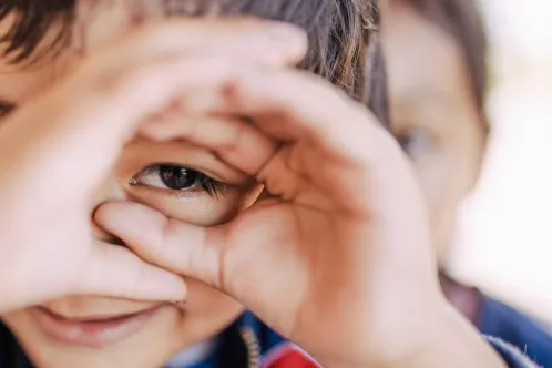 A boy looking through his fingers as if peering through binoculars.