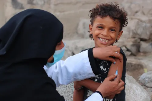 Young child smiling at the camera while getting vaccinated in Yemen.