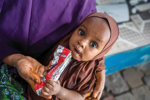 Une jeune fille regarde l’appareil photo en mangeant un sachet d’un aliment thérapeutique appelé le Plumpy’nutMD.