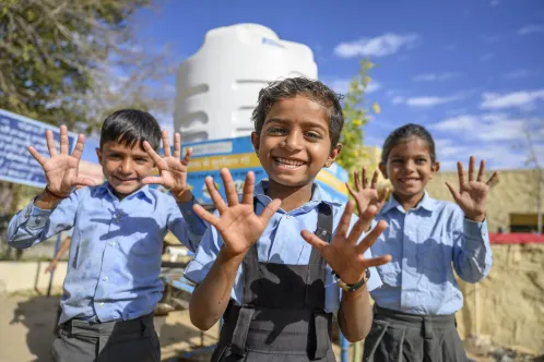 Trois enfants sourient à l’objectif en montrant leurs mains lavées.