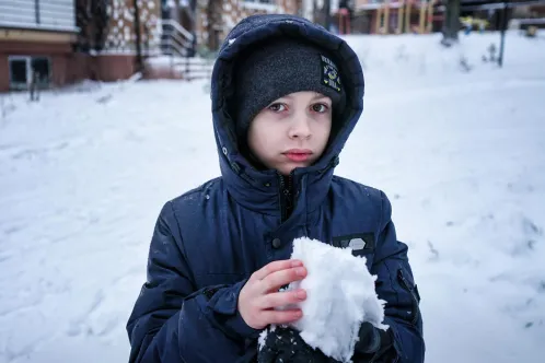 A young boy makes a snowball in Irpin, Ukraine. His home does not have proper heating and electricity, and he is unable to attend school. 