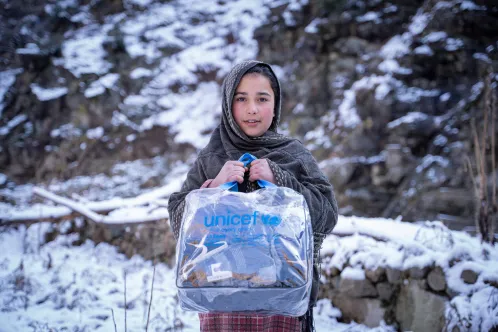 Une jeune fille dans la neige au Pakistan tient un sac à l’effigie de l’UNICEF contenant une couverture et des vêtements.