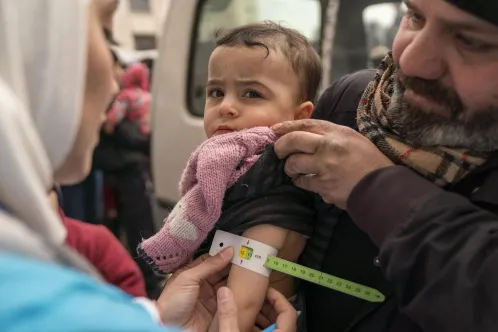 Un membre d’une équipe de santé mobile soutenue par l’UNICEF fait un test de dépistage de la malnutrition sur un bébé dans les bras de son père, en mesurant la circonférence de son bras à l’aide d’un ruban millimétré.