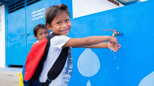 A girl smiles at the camera while washing her hands at a UNICEF tap.