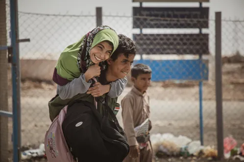 Au Yémen, un garçon porte sur son dos une fille souriante portant un foulard vert. 