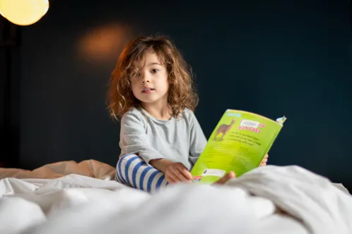 Margot, âgée de 4 ans, lit un livre dans son lit. Comme beaucoup d’enfants, elle est restée à l’écart du service de garde en raison de la pandémie de COVID-19.