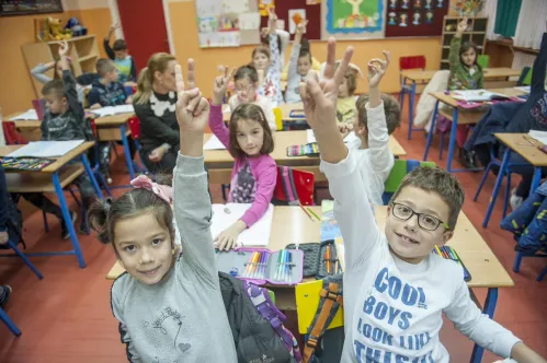 Une salle de classe pleine d’enfants du primaire qui lèvent la main en faisant le signe V pour encourager le vote.