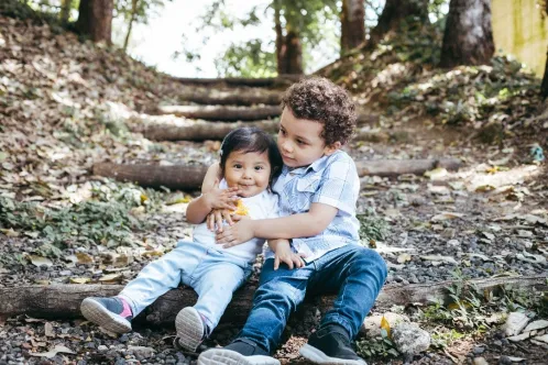 Un jeune garçon est assis dans les bois, enlaçant sa petite sœur par derrière.