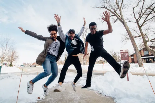 Trois jeunes dehors un jour de neige sautent et posent pour la caméra.