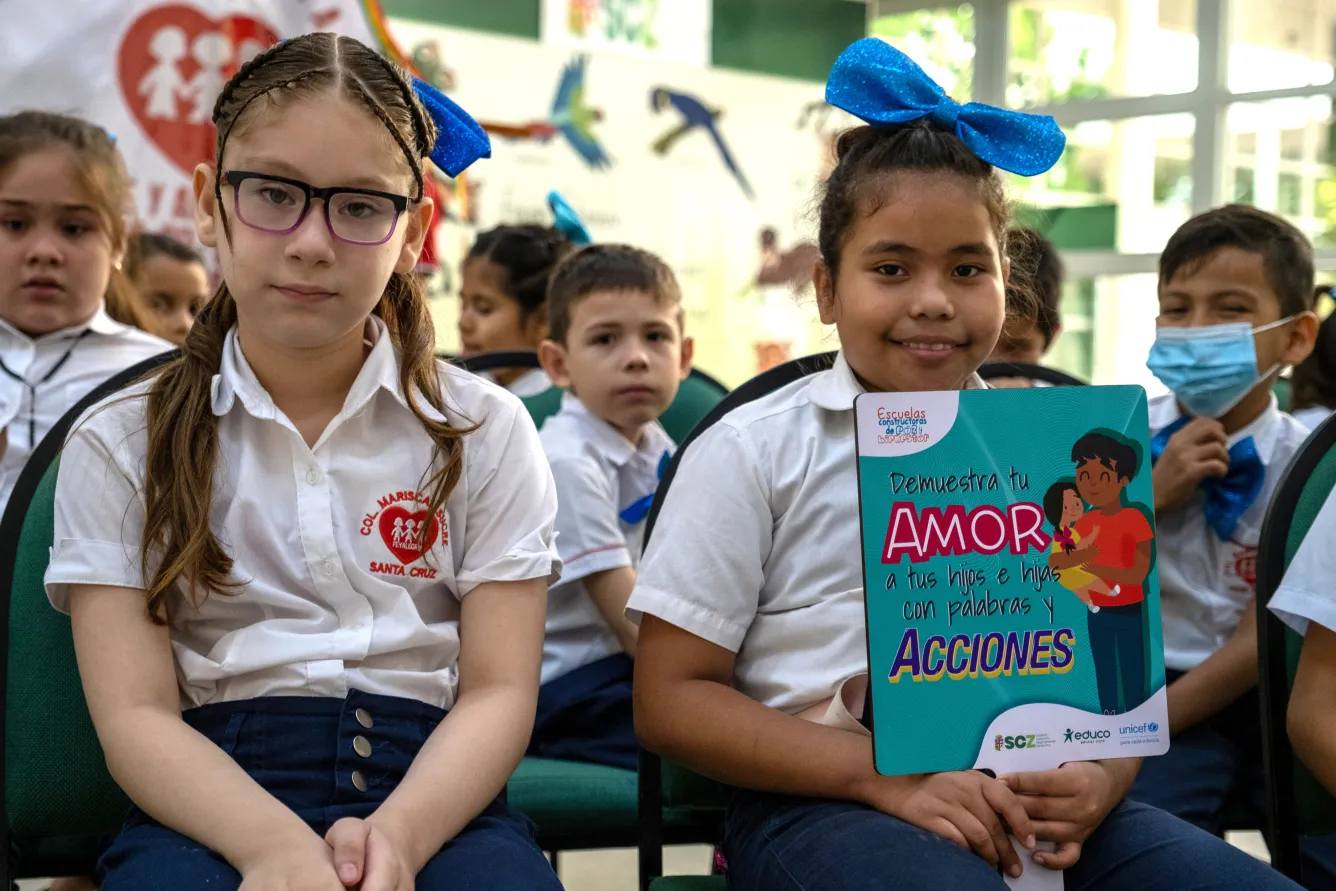 Two girls in uniforms seated in an auditorium as part of a ceremony on prevention of violence against children at a school in Santa Cruz, Bolivia. Both children are looking at the camera.