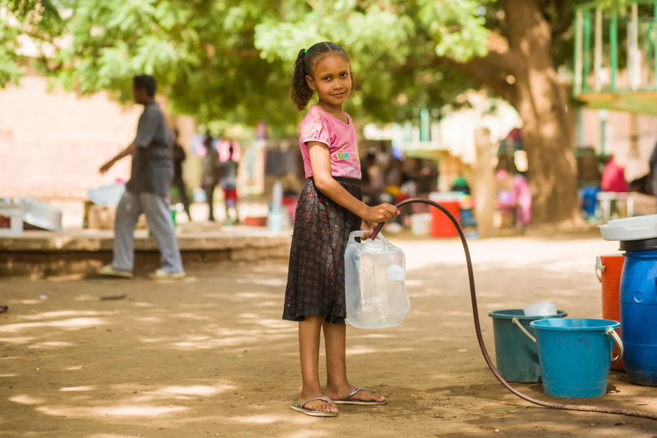 A girls smiles at the camera while collecting water at a gathering point in Sudan.