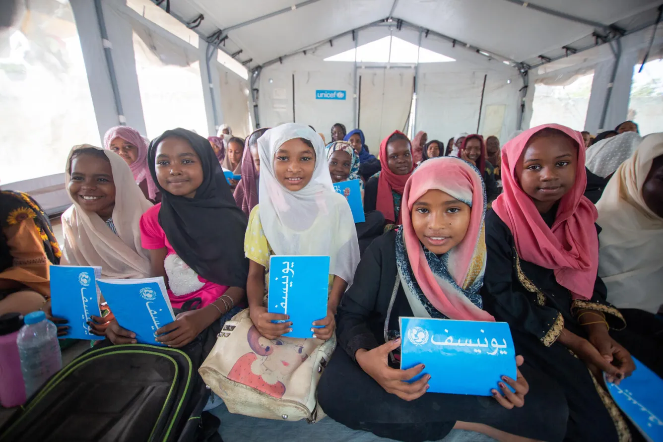 Des enfants munis de cahiers bleus de l’UNICEF sourient à l’objectif dans un espace d’apprentissage sûr soutenu par l’organisme dans l’État de Gezira, au Soudan.