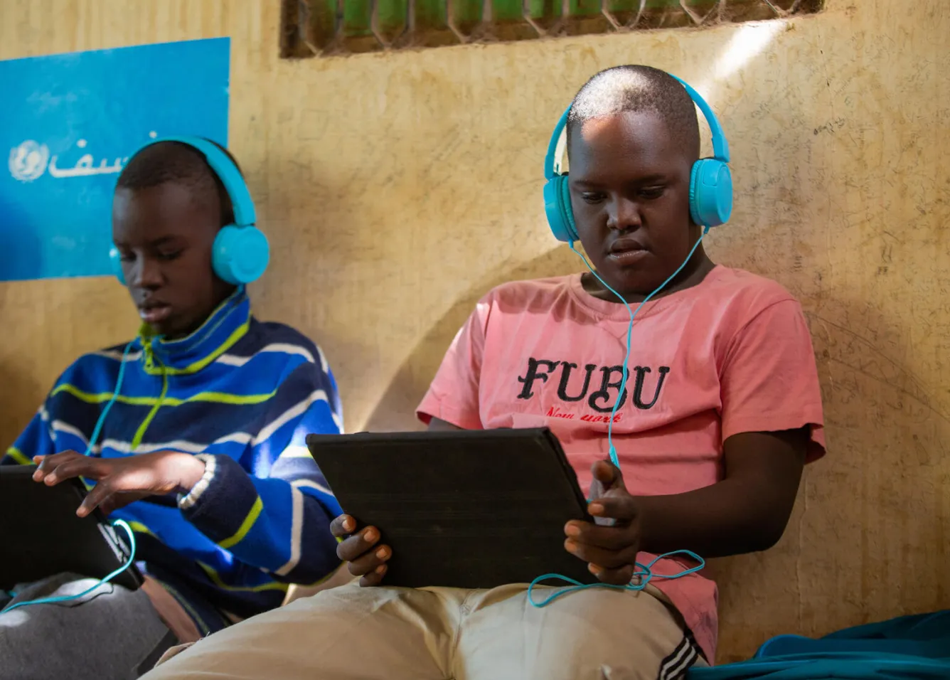 Dans un espace d’apprentissage sûr au Soudan, deux garçons portant des écouteurs se servent de tablettes pour s’instruire.