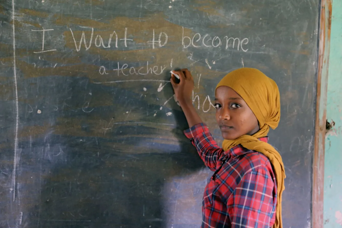 Dans une salle de classe en Éthiopie, la jeune Zemzem, âgée de 13 ans, regarde l’objectif alors qu’elle se tient devant un tableau sur lequel elle a écrit : « Je veux devenir enseignante ».