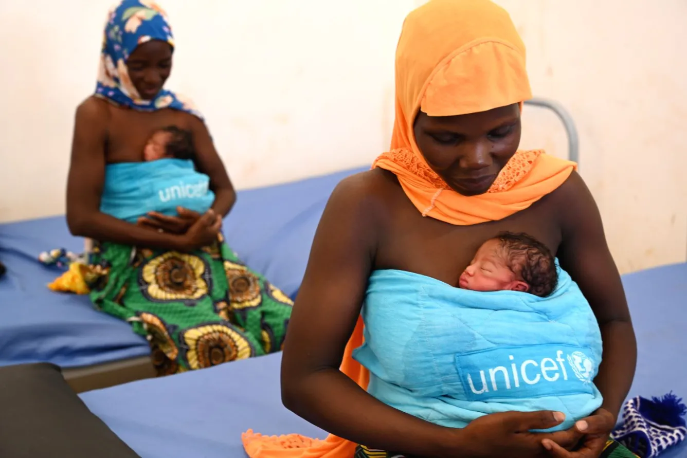 Dans un hôpital du Burkina Faso, deux mères tiennent contre leur poitrine leur bébé enveloppé dans une couverture de l’UNICEF.
