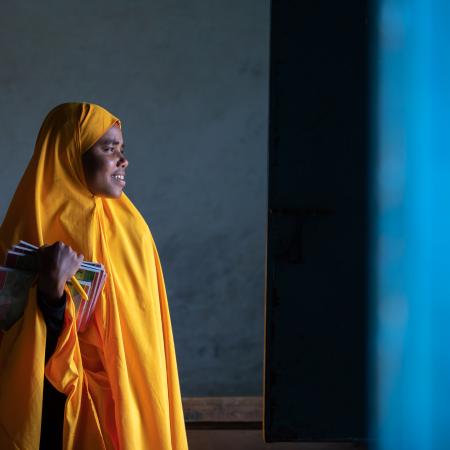 A girl wearing yellow uniform in Somalia looks hopefully into the light 