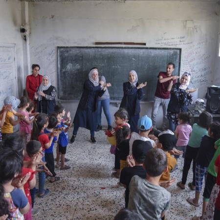 Young children participate in a group activity led by adults at a UNICEF-supported collective shelter in Syria.