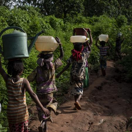 Des enfants marchent sur un chemin dans la forêt, portant des seaux sur la tête, pour puiser de l'eau d'une source naturelle au camp d'Elevage à Bambari, en République centrafricaine