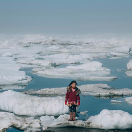 En Alaska, aux États-Unis, une jeune fille vêtue d'un manteau rouge se tient debout sur une banquise.