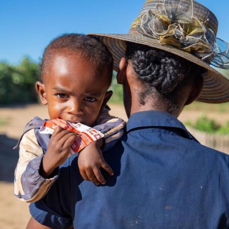 A young boy eating PlumpyNut® in his mother’s arms.