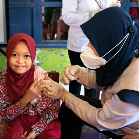 A girl looks at the camera as a nurse administrators an injection to her arm.