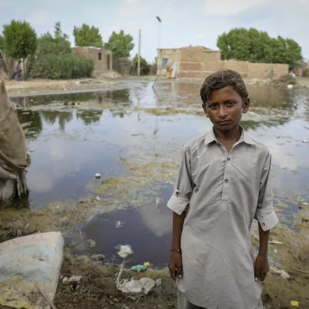 A child looks into the camera, behind him are a flooded field and half submerged homes.
