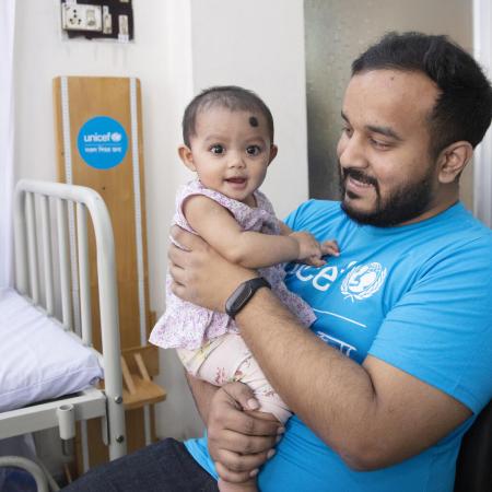 Un employé de l’UNICEF tient une petite fille dans ses bras dans une clinique soutenue par l’organisme au Bangladesh.