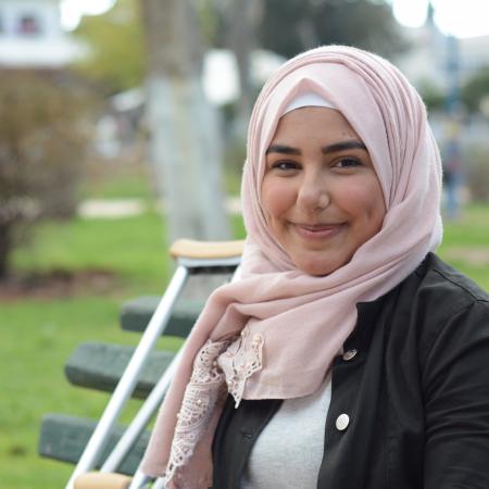 Nour sitting on a bench with her crutches beside her.