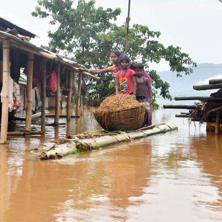 A woman carries straw for her cattle on a raft through flood waters at Sarumariparvat village in Morigaon district on July 22, 2020. Photo by Biju Boro