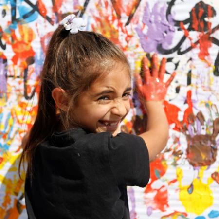 Dans un centre soutenu par l’UNICEF en Türkiye, une fille souriante pose ses mains couvertes de peinture sur un mur d’empreintes colorées.