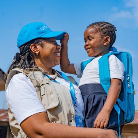 In the Democratic Republic of the Congo, A UNICEF worker carries a child wearing a blue UNICEF backpack.