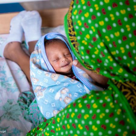 An infant wrapped in a towel smiling in the lap of its parent 