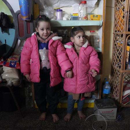 Two girls wearing pink winter clothes stand beside each other. One girl smiles at the camera. 