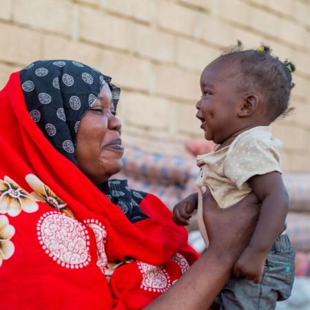 In Sudan, a smiling mother holds up her 10-month-old daughter.