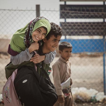 Au Yémen, un garçon porte sur son dos une fille souriante portant un foulard vert.