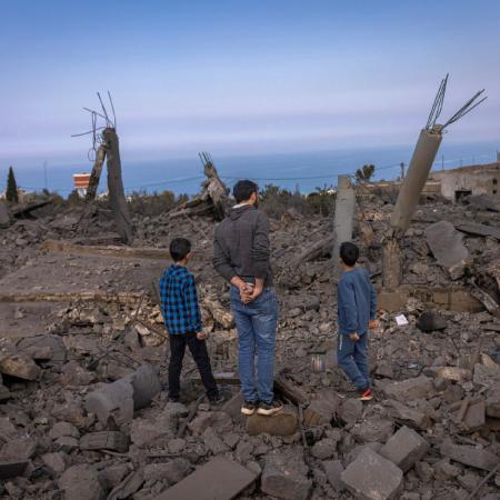 Au Liban, deux enfants et un adulte tournent le dos à l’objectif au milieu de tas de décombres.