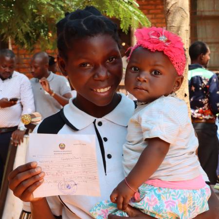 A mother holds her child lovingly while also showing the child's birth registration certificate. 